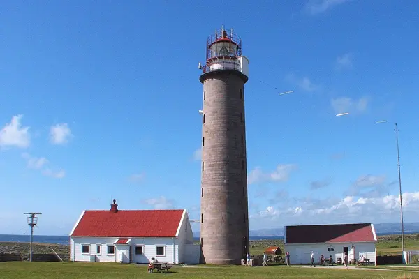 Lista fyr, et steinfarget fyrtårn , med rød metallramme rundt lykten øverst og besøkssenteret i to hvite lave hus på hver side av fyret