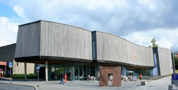 Forsiden på Lillehammer Kunstmuseum, en svakt buet betongvegg som stikker ut over en glassfasade med inngangsparti