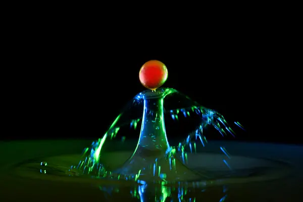 En fargerik ball balanserer på toppen av en opplyst vannsprut, fanget i et eksakt øyeblikk med mørk bakgrunn
