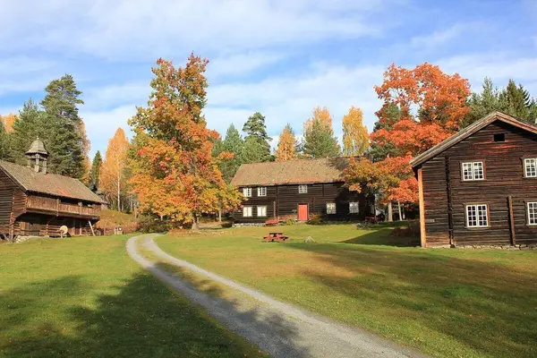 Tun med låve med tårn på den ene siden, kårstue på den andre og hovedhuset i midten, fotografert en høstdag med rødgule blader bjørketrærne bak tunet