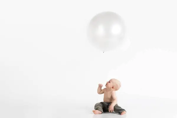 En liten gutt sittende på gulvet i et hvitt rom iført grønne bukser og som ser opp på en stor hvit ballong som illustrasjon til St.Croix-huset i Fredrikstad