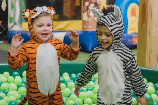 To små barn i tiger- og sebradrakter leker sammen i et basseng fylt med grønne baller som illustrasjonsbilde for beskrivelsen av Lekeland Drammen