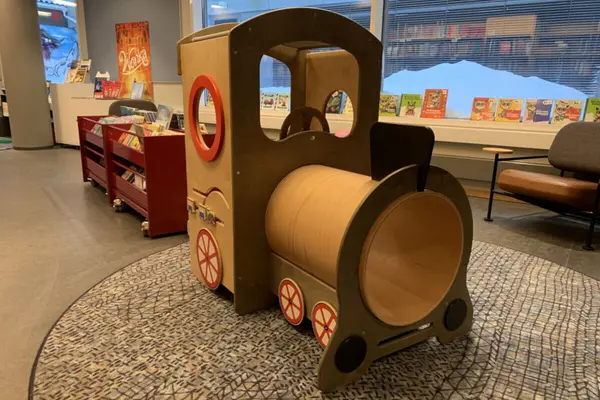 Interiør fra Bærum bibliotek Sandvika, et lokomotiv i finér på et teppe og flere hyller og karmer med bøker