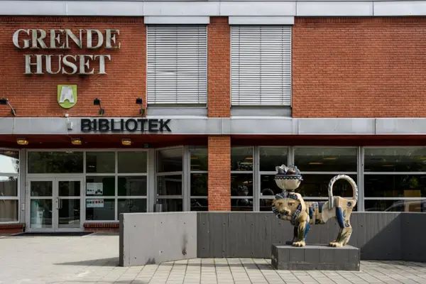 Inngangen til Bærum bibliotek Rykkinn, mursteinshus med Grendehuset og bibliotek i bokstaver på veggen, glassparti og en løveskulptur foran