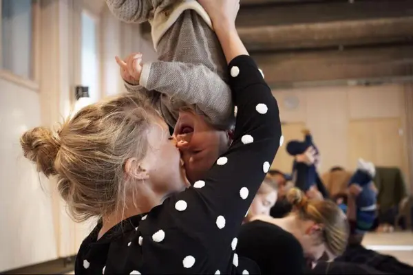 En kvinne løfter en smilende baby opp ned under en babydans-aktivitet