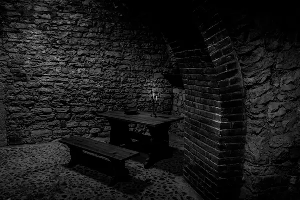 Et mørkt, steinbelagt kjellerrom med et enkelt trebord, benk og en lysestake, som illustrasjonsbilde for beskrivelsen av omvisning i kjeller og krypt i Nidarosdomen.