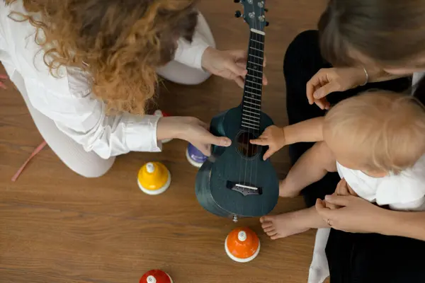 En baby får hjelp av voksne til å spille på en liten gitar under en musikkaktivitet, som illustrasjonsbilde for beskrivelsen av Musikklek på Sølvberget