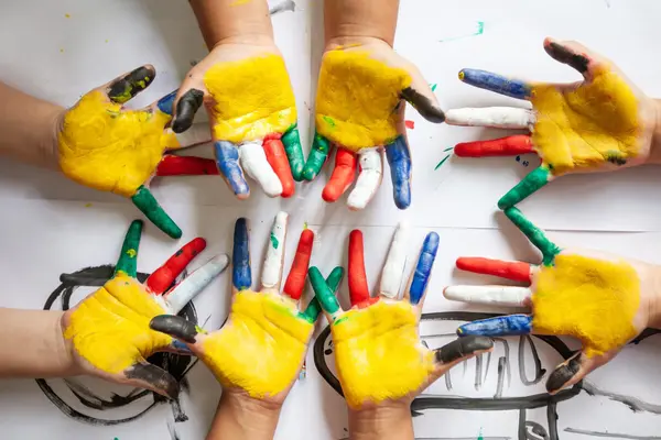 Barns hender malt i sterke farger med gul maling i håndflatene og regnbuefargede fingre som illustrasjonsbilde for beskrivelsen av Familielørdag på Kunstnernes Hus 