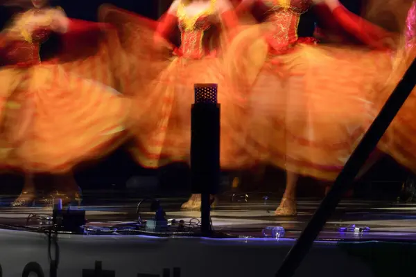 Uskarpt bilde av dansere i fargerike, røde og gule kjoler som snurrer på scenen som illustrasjon til beskrivelsen av Familieforestillinger og teater for barn i Stormen Konserthus