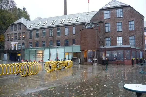 USF Verftet, en bred og høy mursteinsbygning med noen glassfasader på bakkeplan og en stor plass utenfor med gule sykkelstativer som illustrasjon for familiedager på USF Verftet