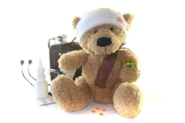 Tøybamse med bandasje rundt hodet og nesedråper ved siden av seg mot en hvit bakgrunn, som illustrasjonsbilde for bamsehospital på KUBEN Arendal
