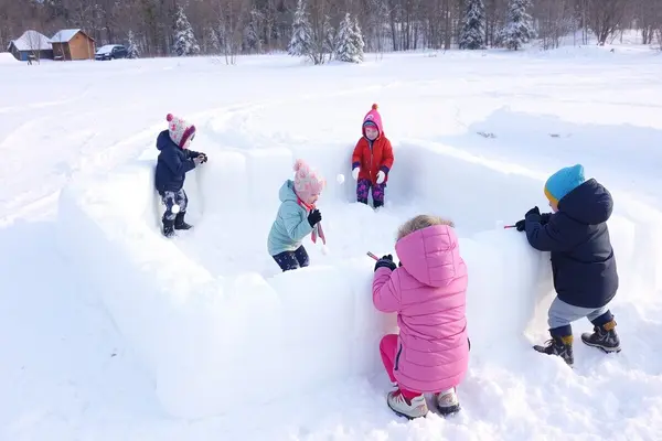 Barn leker ute i vinterlandskap og bygger en rund snøborg av store snøblokker sammen, som illustrasjonsbilde for vinterferieaktiviteter på Maihaugen