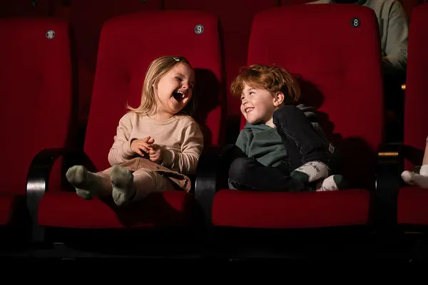 To små barn ler sammen i røde kinoseter under en filmvisning på kino, som illustrasjonsbilde for beskrivelsen av Barnas Cinematek og barnefilm i helgene