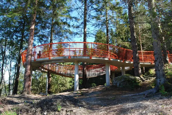 Rund oransje installasjon som man kan løpe på, bygget med trær inni og en gangbro, et av seks naturrom bygget for barn langs Løvstien i Bergen