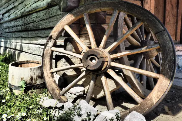 Et vognhjul i tre lent opp mot tømmeret på en gammel bygning, som illustrasjonsbilde for beskrivelsen av Sensommerdag på Hordamuseet