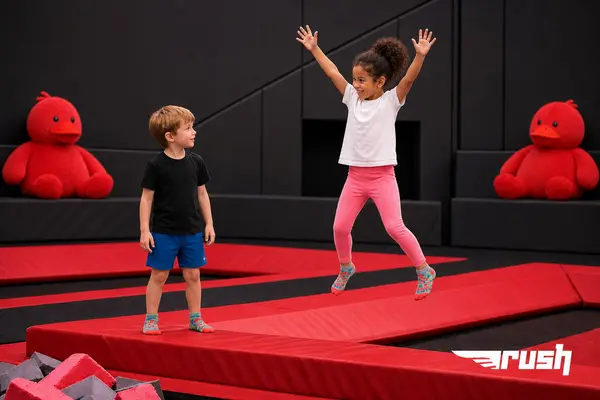 En jente som hopper på en trampoline og en gutt som ser på henne mot en svart bakgrunn, som illustrasjonsbilde for beskrivelsen av Rush trampolinepark Bergen