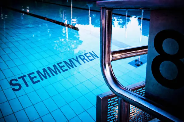 Innendørs svømmebasseng, bilde av deler av vannspeilet og en startkloss med nummer åtte på siden og STEMMEMYREN skrevet med store bokstaver på bunnen, som illustrasjonsbilde for beskrivelsen av Stemmemyren svømmehall