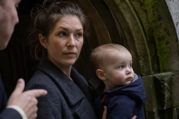 Mor med baby i favne som lytter til en omviser i en borglignende buegang, som illustrasjonsbilde for beskrivelsen av babyomvisning i Håkonshallen i Bergen