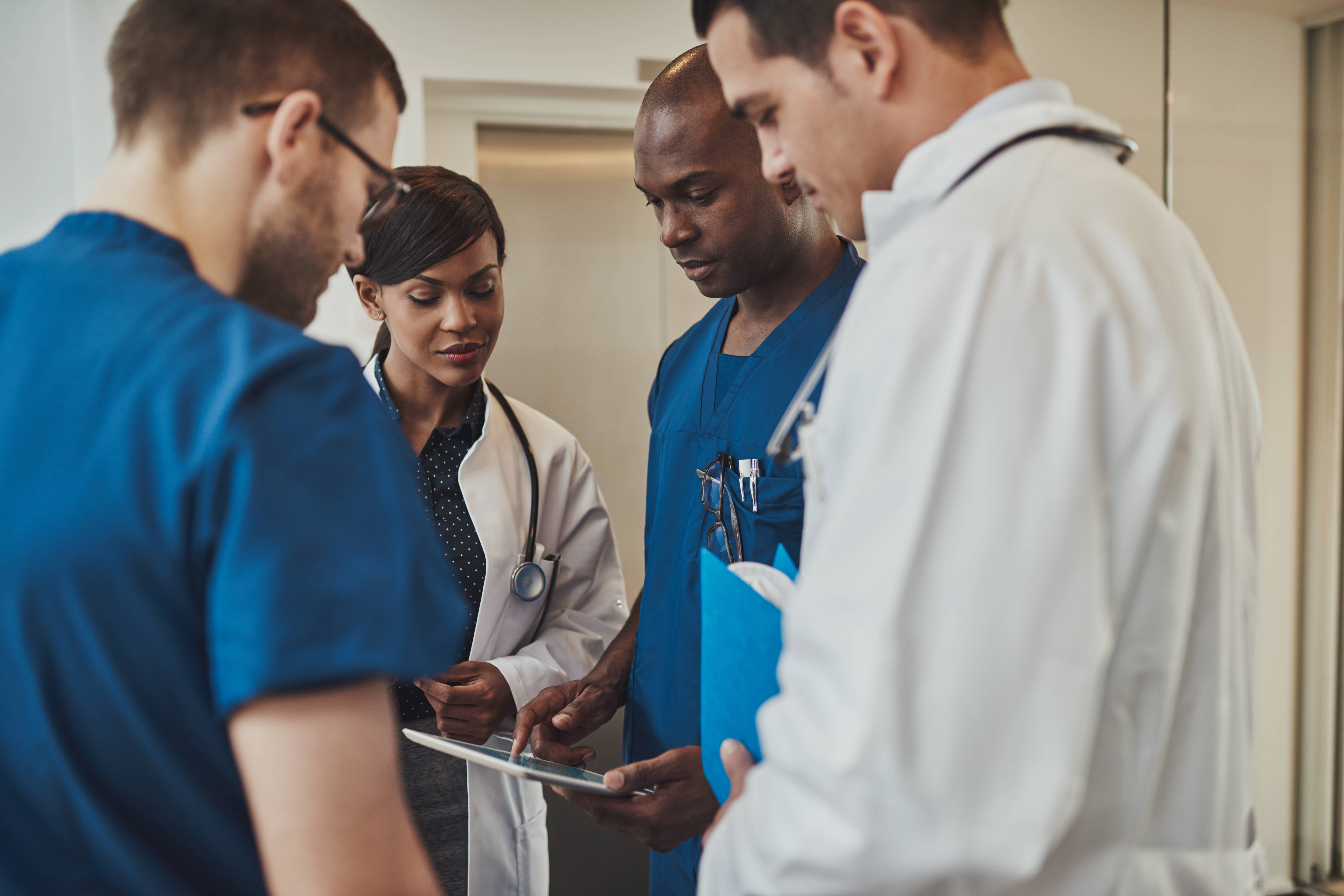 Four medical professionals reviewing information on a tablet during a discussion in a clinical setting.
