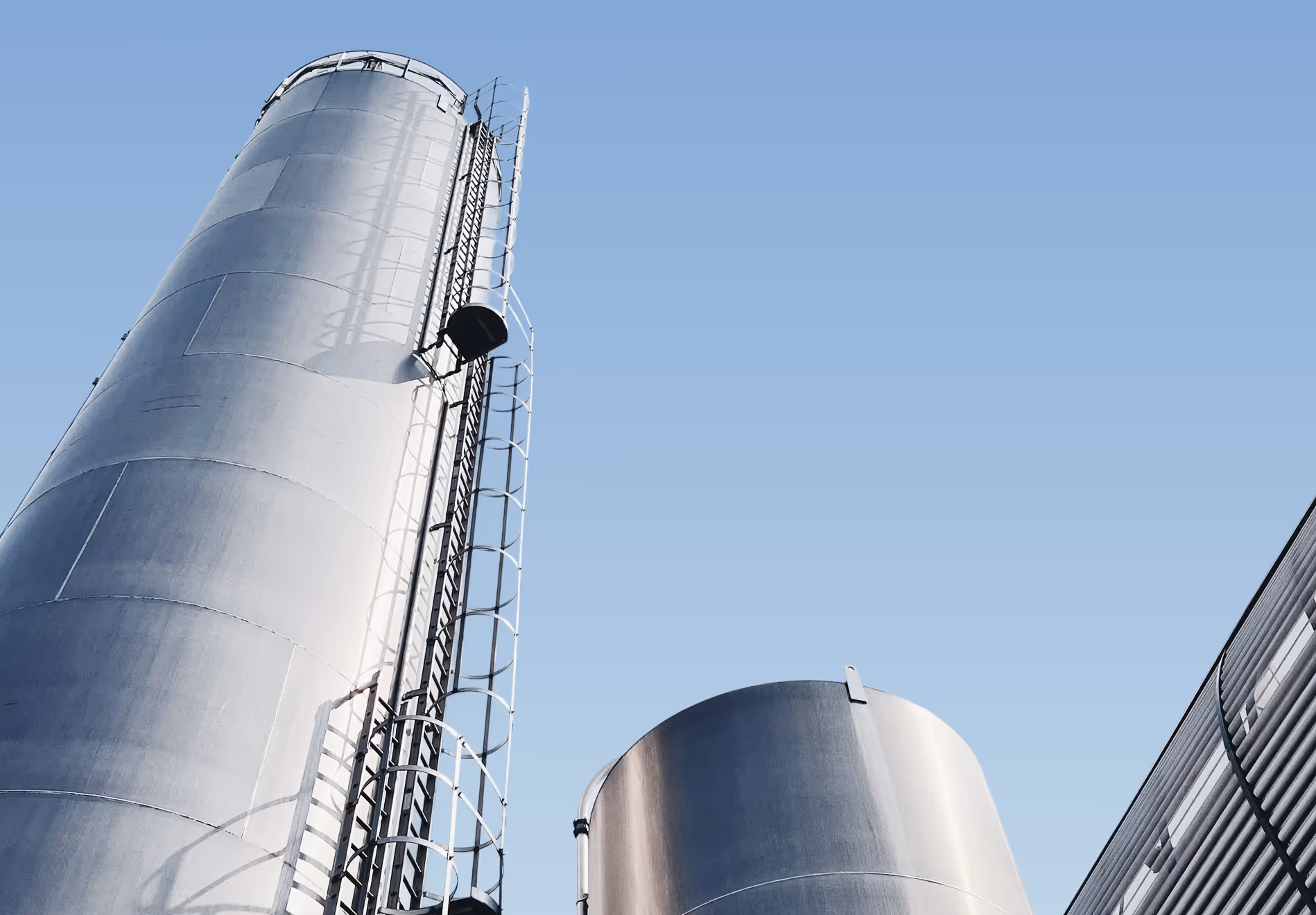Two large metallic industrial storage tanks with ladders against a clear blue sky.