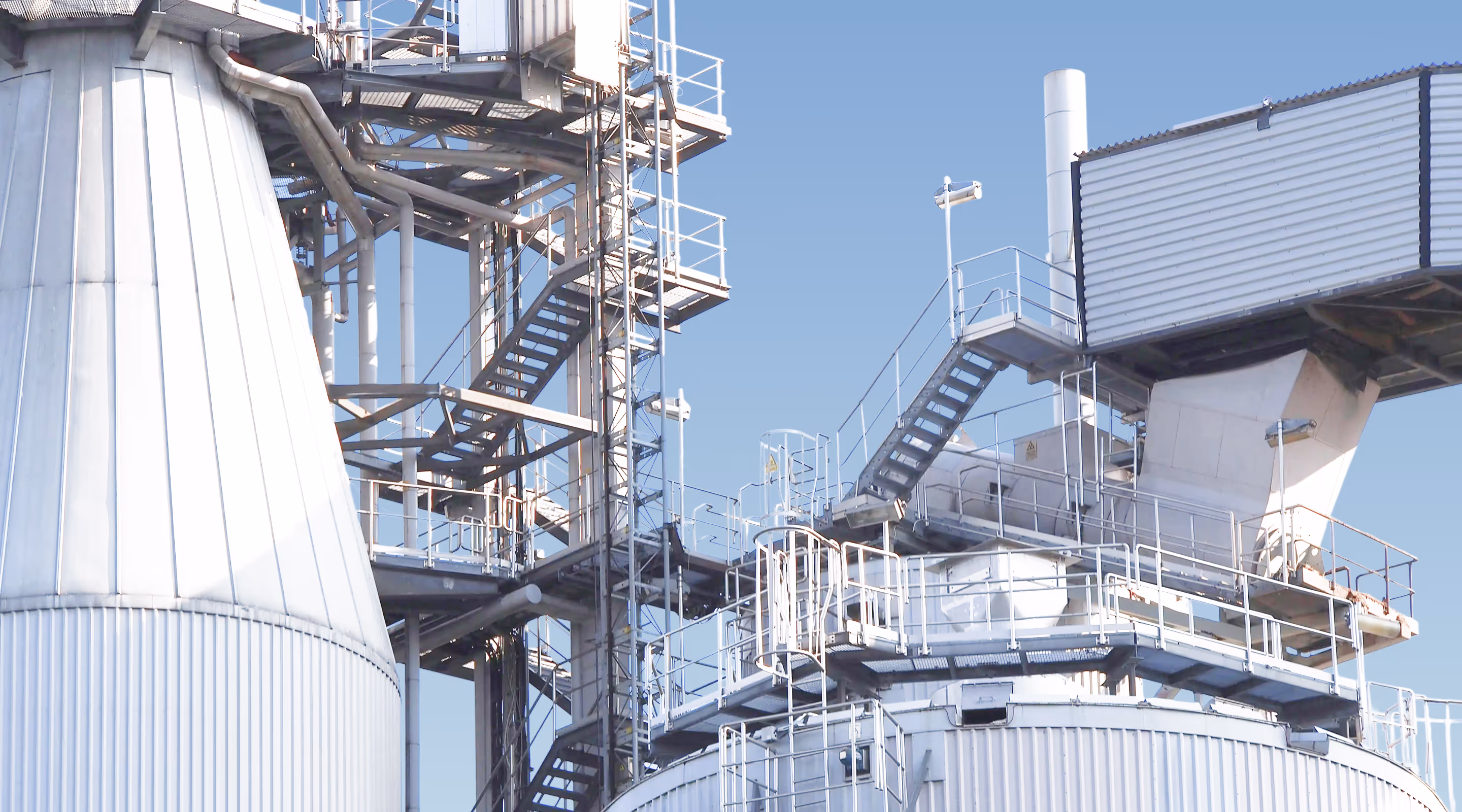 Industrial metal structures with staircases and platforms against a clear blue sky.