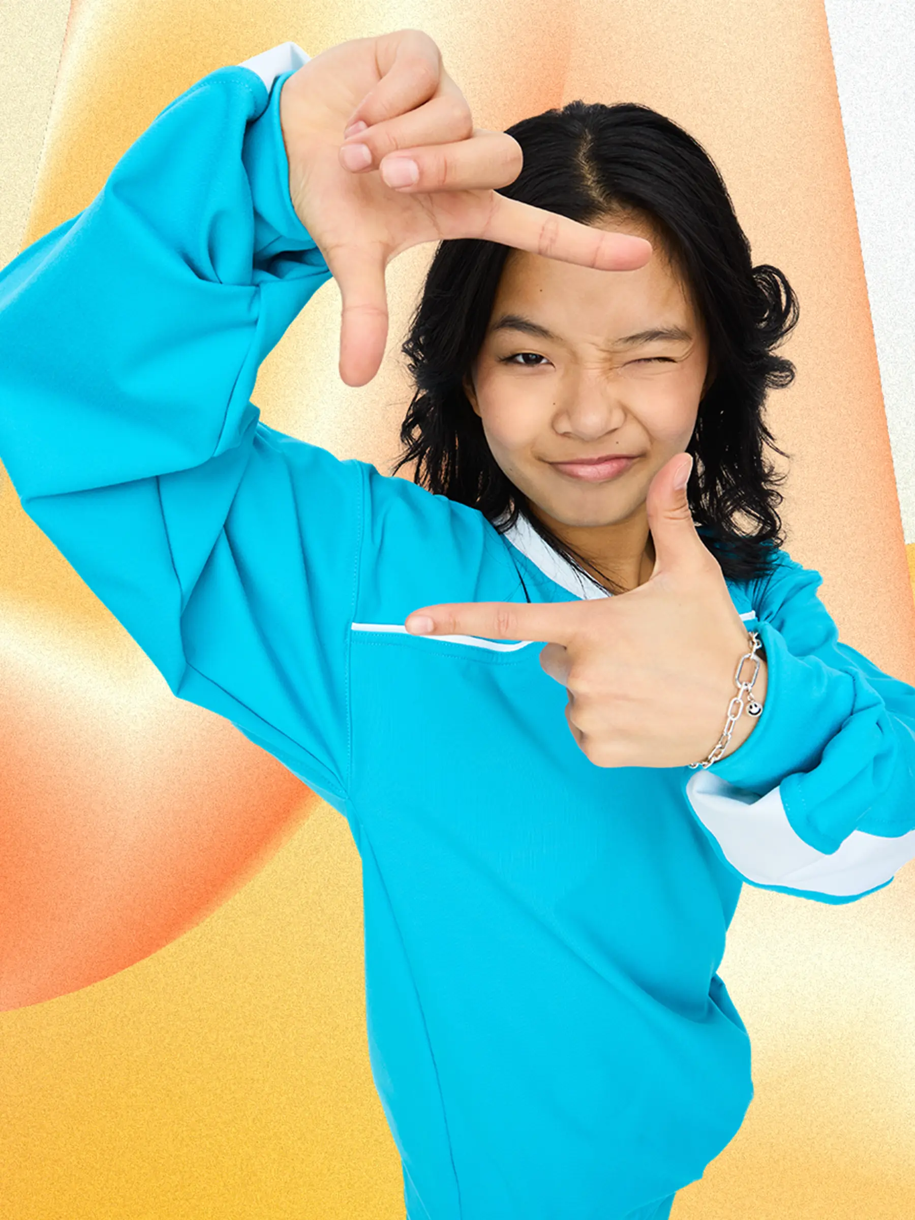 Young person in a blue jacket making a rectangle frame with their fingers and winking.