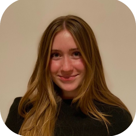 Smiling woman with long light brown hair wearing a black top against a plain beige background.