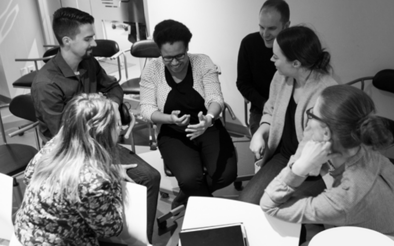 Group of six people sitting in a circle engaged in a lively discussion in an office setting.