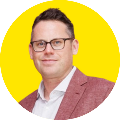 Man wearing glasses and a red blazer with a white shirt against a yellow background.