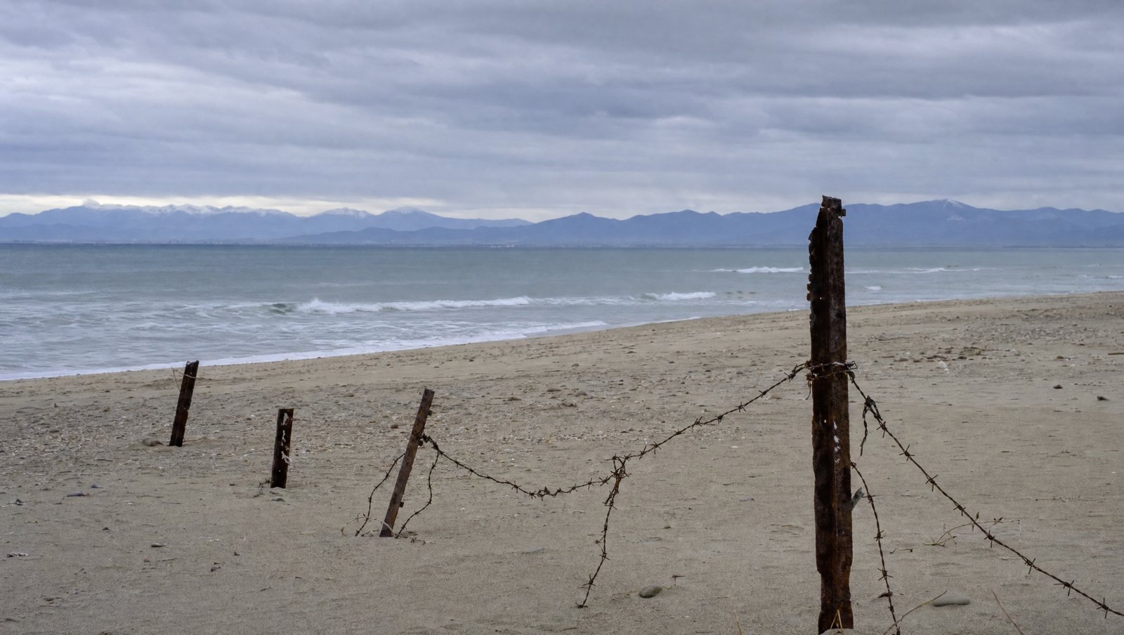 Plage déserte en hiver, vestiges de barbelés rouillés dans le sable et mer grise
