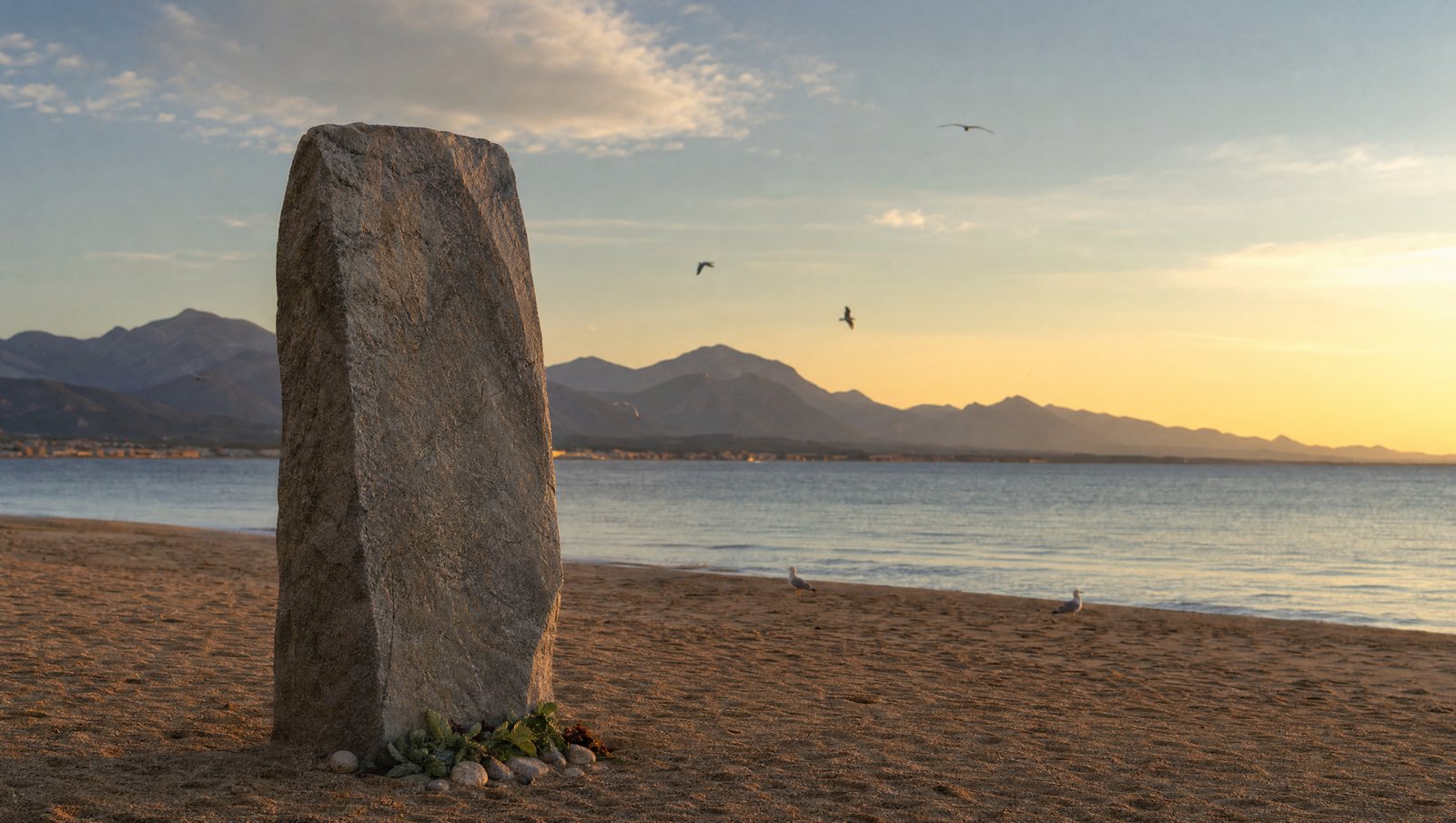Monolithe commémoratif sur une plage face à la Méditerranée au crépuscule