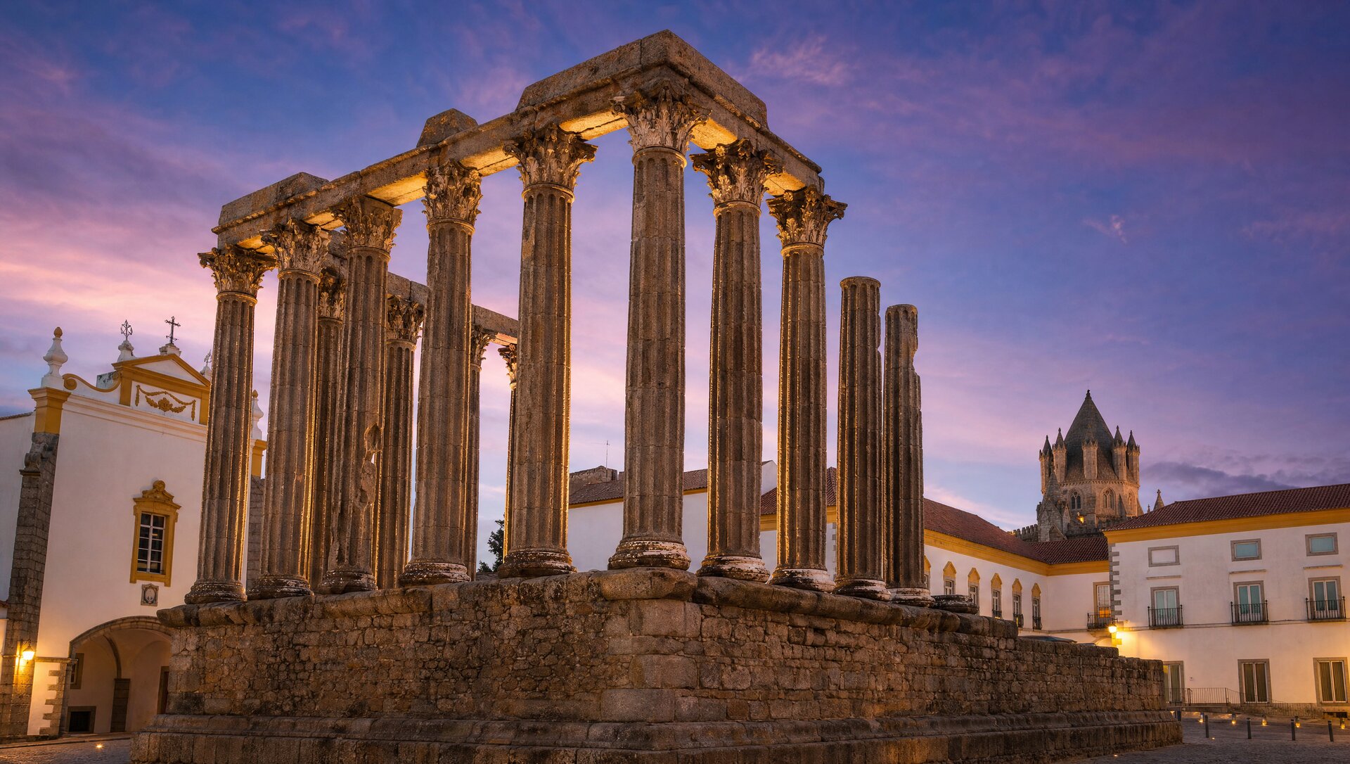 Temple romain d'Évora dit temple de Diane au crépuscule, colonnes corinthiennes de granit dressées contre un ciel violet, éclairage doux mettant en valeur les pierres antiques