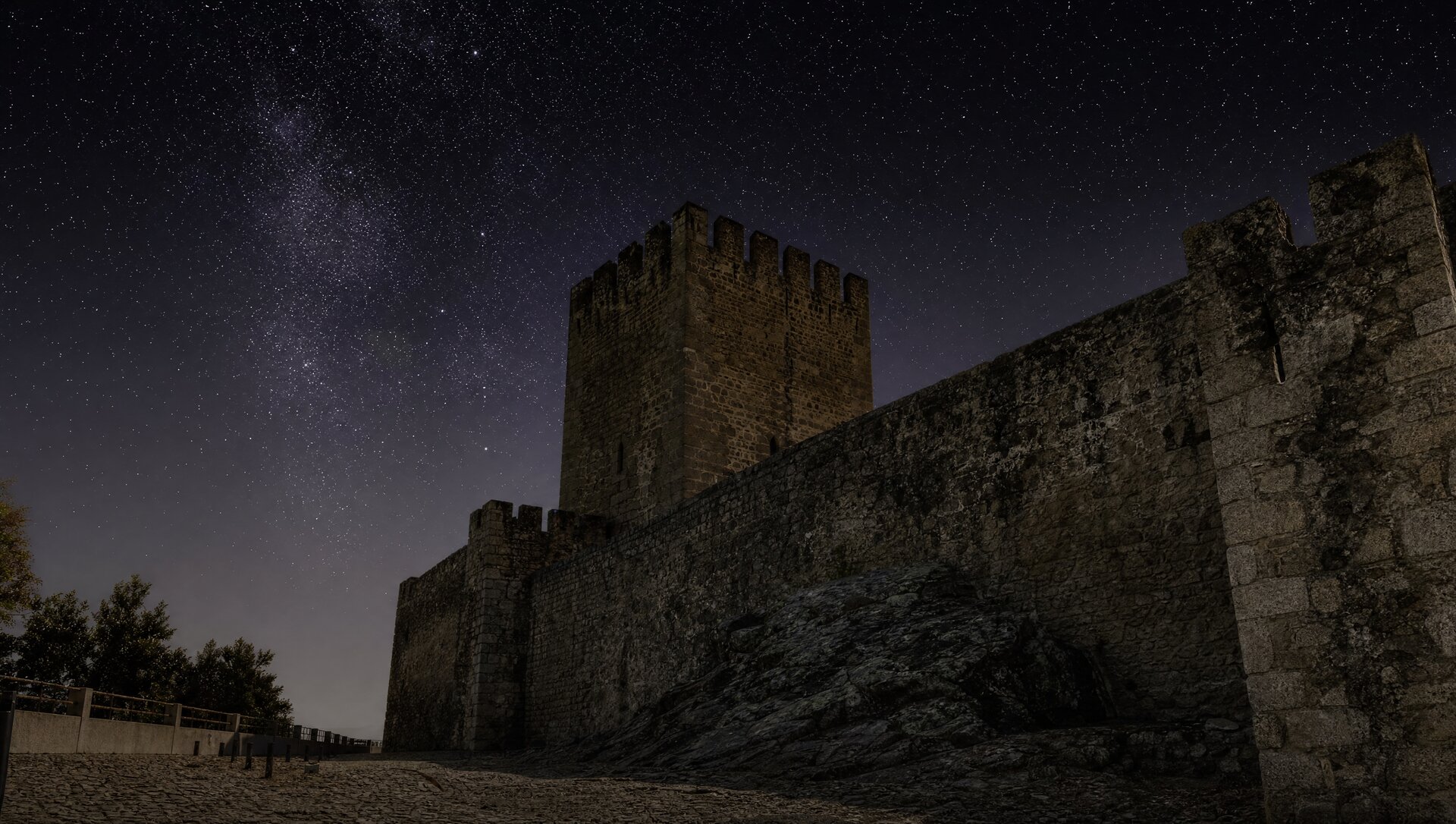 Anciennes murailles de pierre d'Évora sous un ciel de nuit étoilée, tour de garde médiévale se découpant en silhouette sombre, ambiance tendue et minérale de guet nocturne