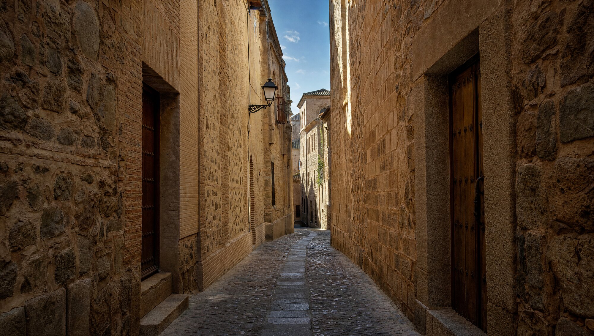 Ruelle médiévale pavée de la vieille ville de Tolède, aux hauts murs de pierre dorée