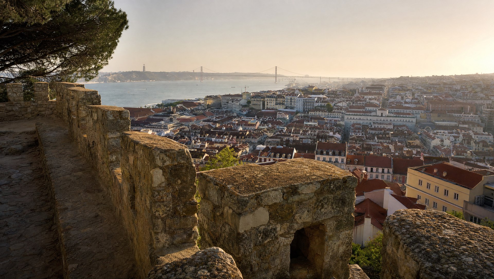 Remparts du Castelo de São Jorge dominant les toits de Lisbonne et le Tage argenté en contrebas, ciel de fin de journée