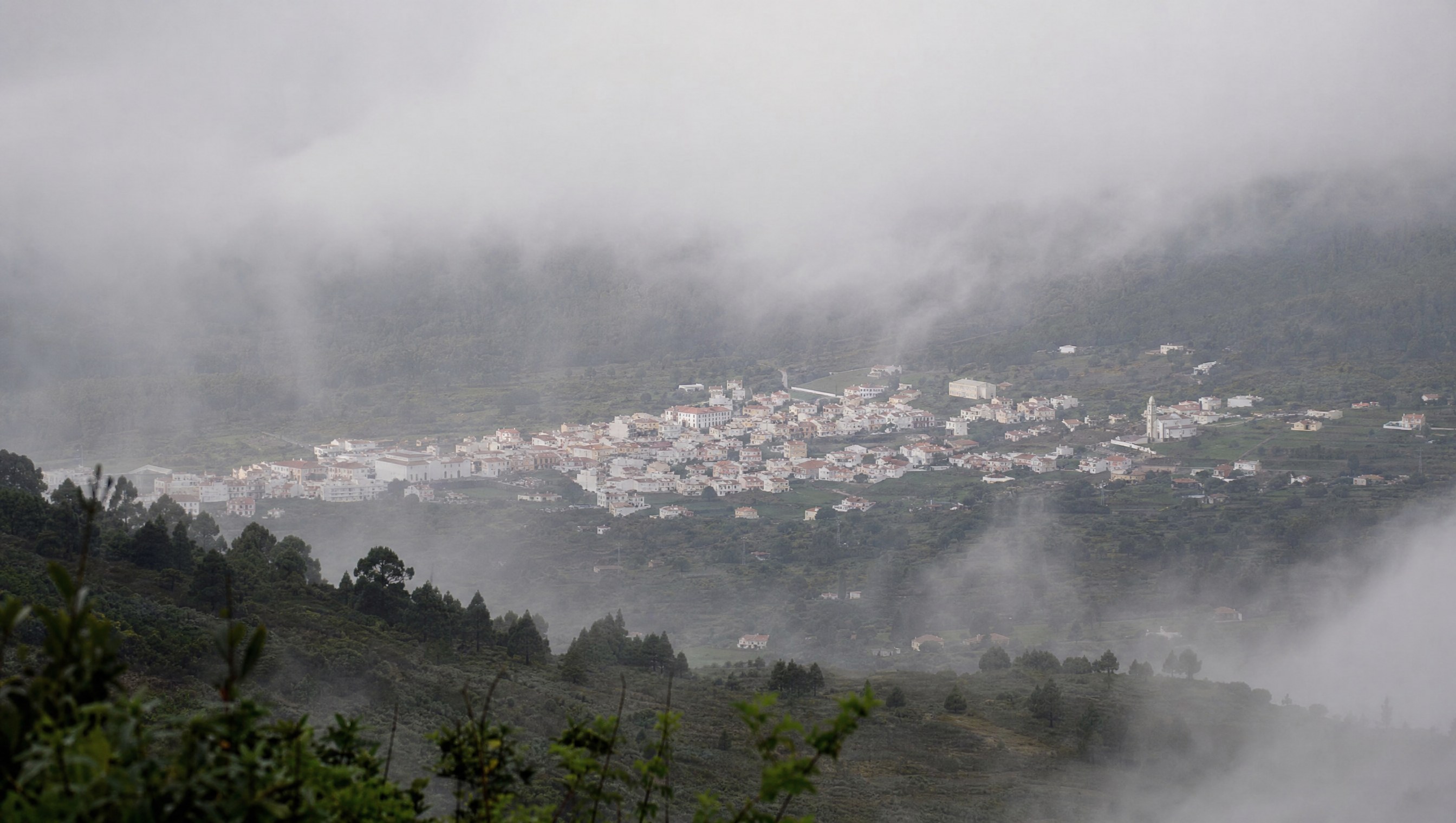 Vue de la ville de Valverde, capitale d'El Hierro, blottie à l'intérieur des terres à flanc de vallée volcanique, toits clairs sous une brume d'altitude, lumière grise et douce du matin