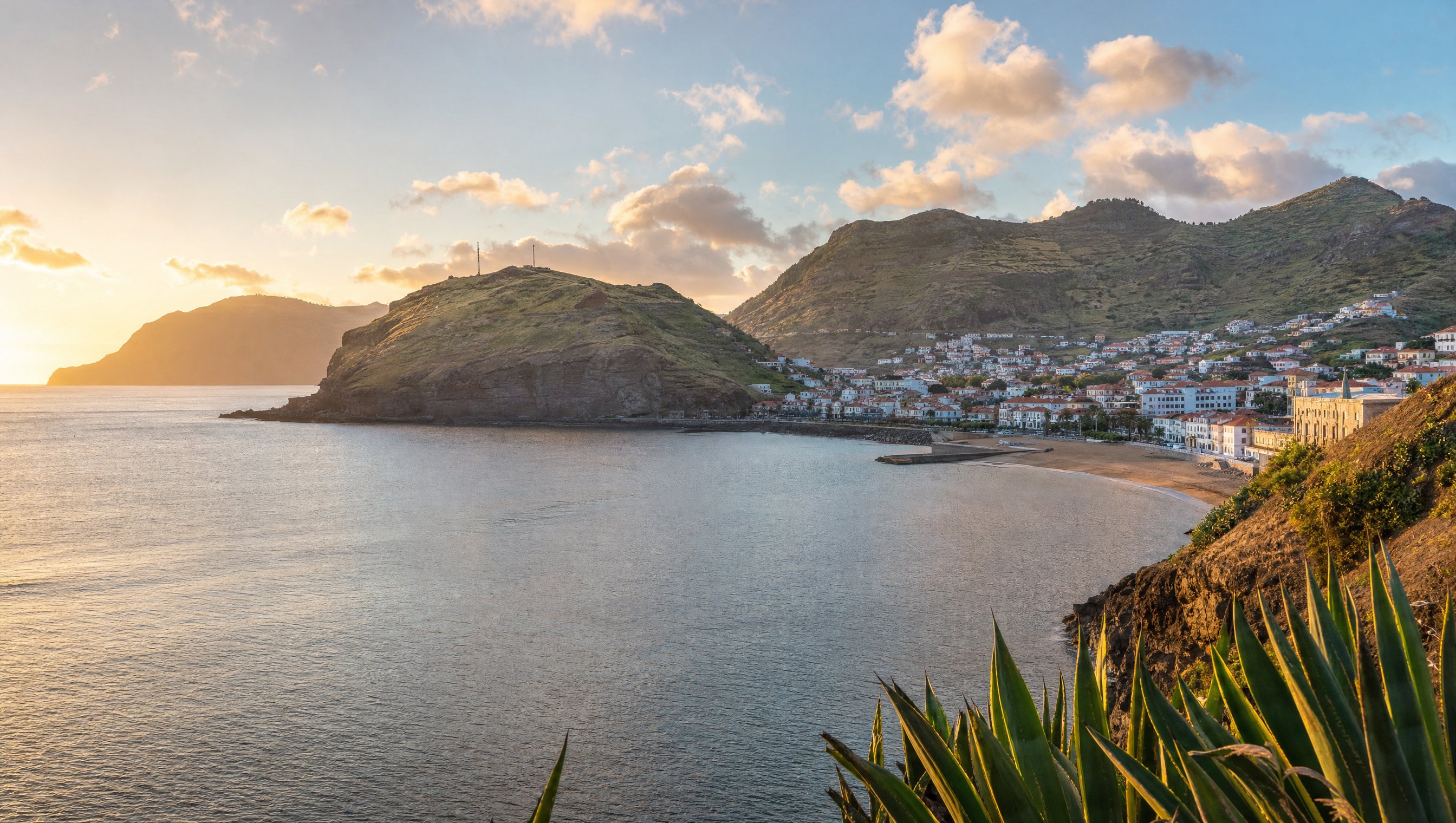 Baie abritée de Machico au petit matin, mer calme, collines vertes en arrière-plan, lumière dorée oblique, photographie éditoriale de voyage