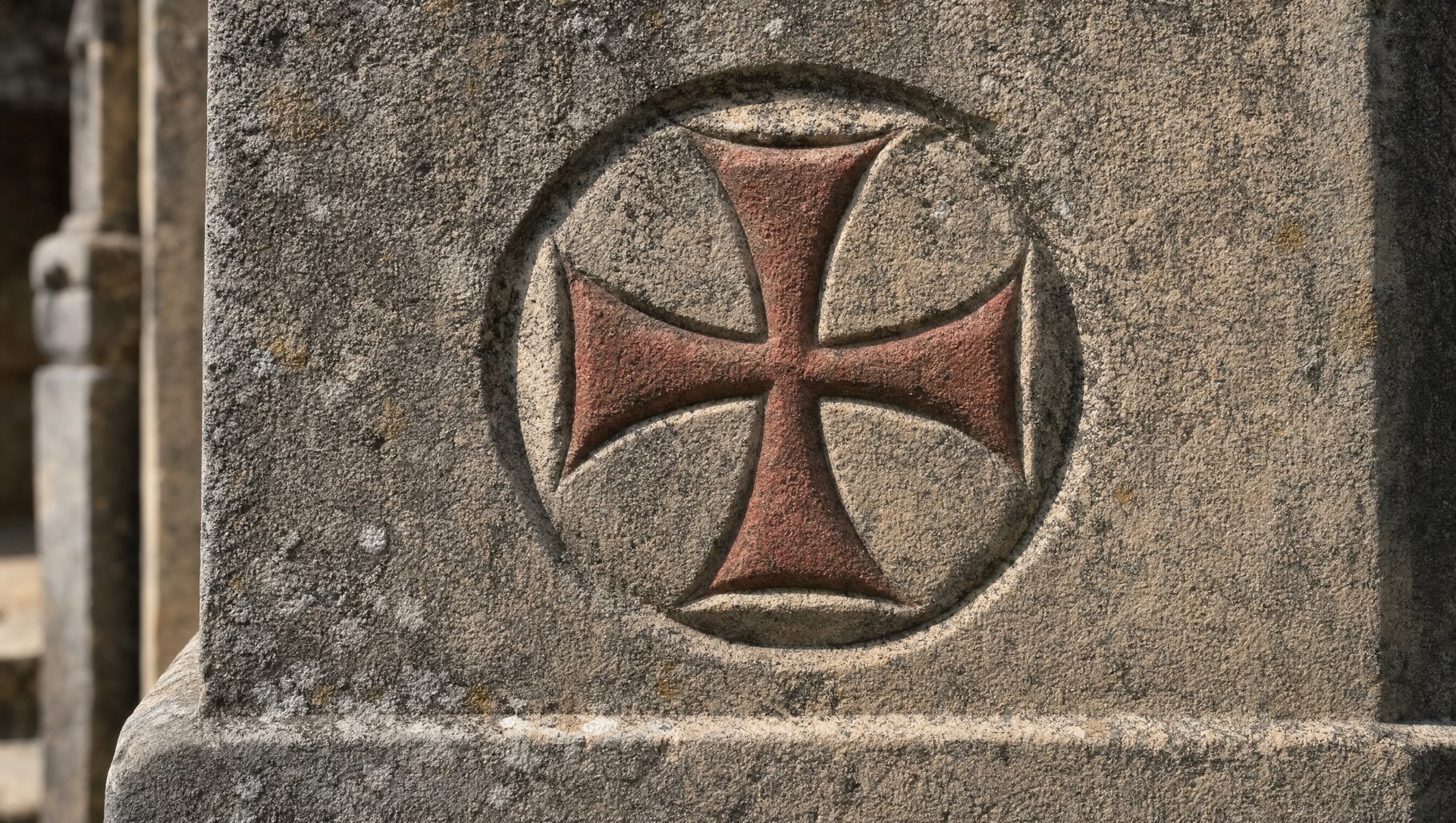 Une croix rouge pattée de l'Ordre du Christ sculptée dans la pierre du couvent de Tomar, gros plan, granit patiné, lumière rasante, évoquant la filiation directe avec la croix templière
