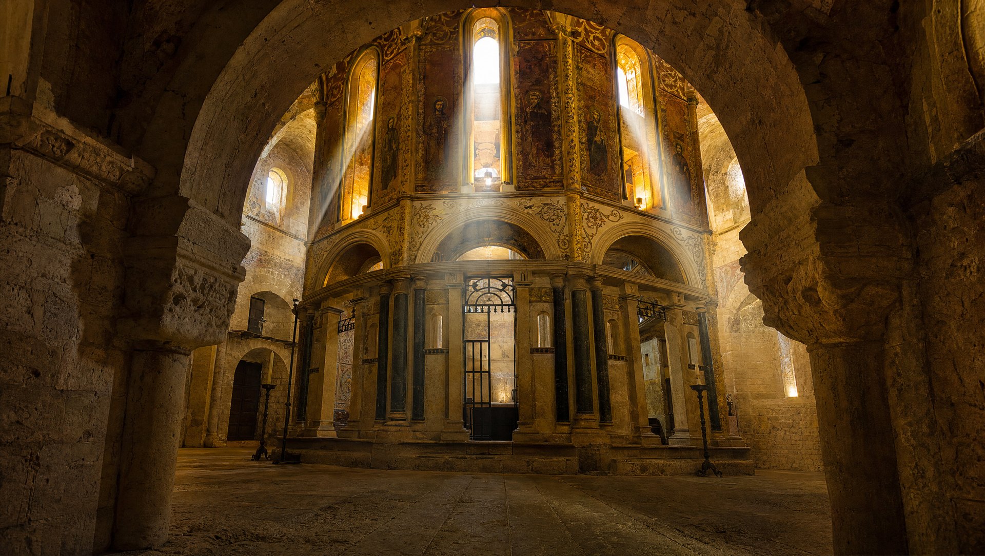 La Charola de Tomar, rotonde romane à seize pans inspirée du Saint-Sépulcre de Jérusalem, chœur octogonal central, murs couverts de peintures et de dorures, faisceaux de lumière tombant des hautes fenêtres, atmosphère de forteresse-sanctuaire