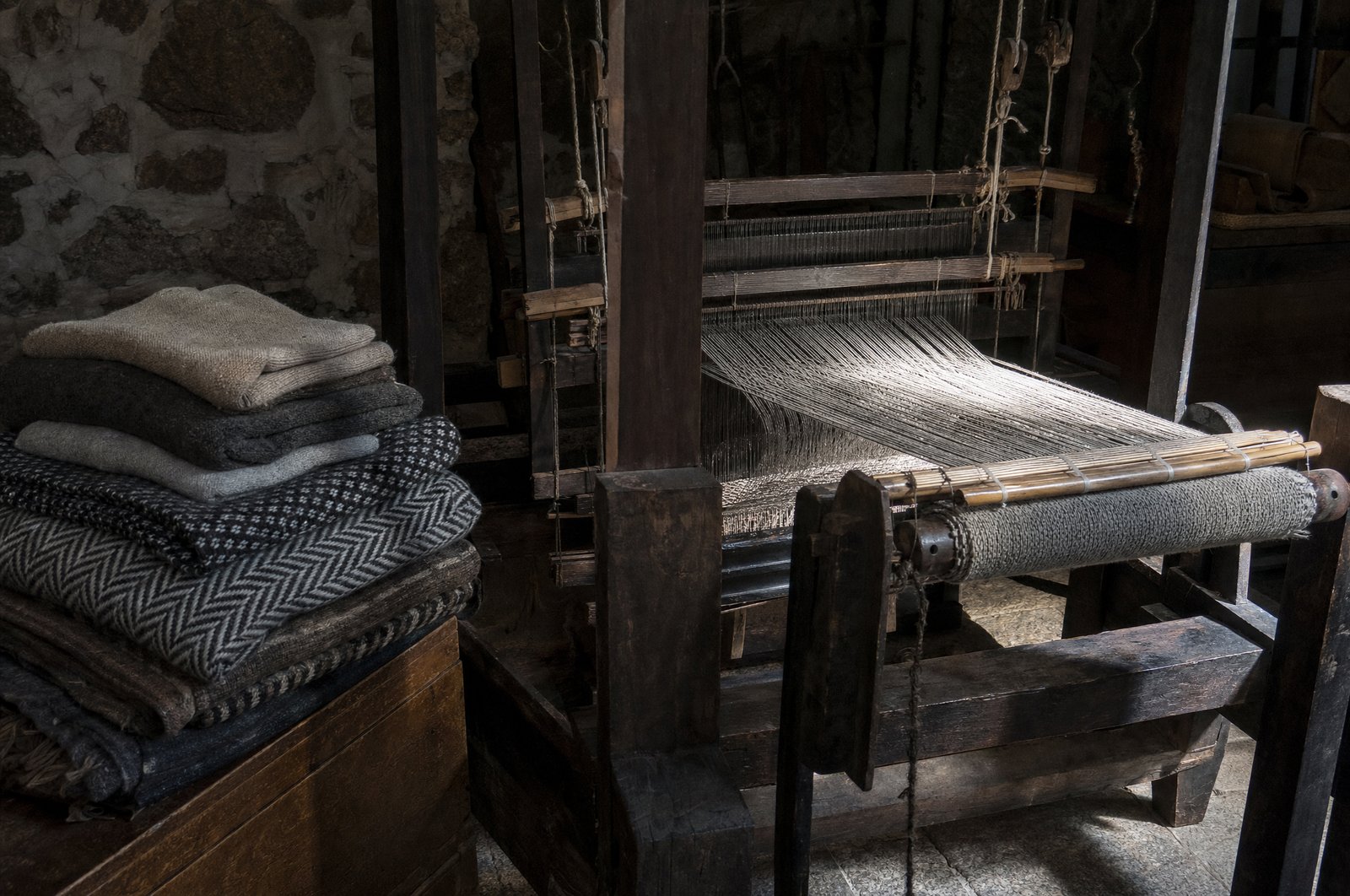 Vieux métier à tisser en bois et pièces de drap de laine dans la pénombre du musée de la laine de Covilhã, faisceau de lumière sur les fils tendus, atmosphère d'atelier ancien, sans personne