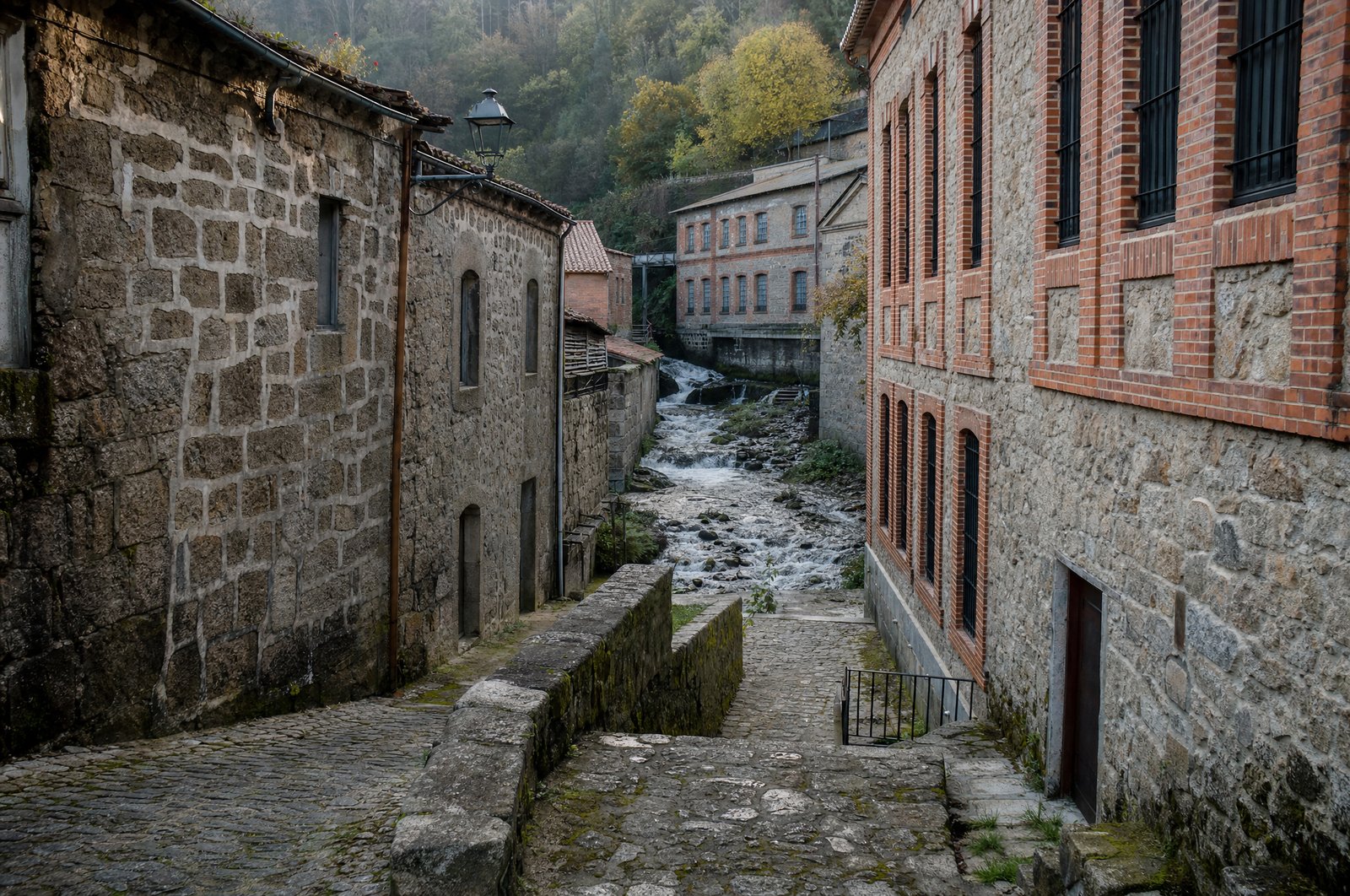 Ruelles en pente de la vieille Judiaria de Covilhã, façades de granit et de brique d'anciennes fabriques de laine le long d'un ruisseau de montagne, lumière froide de novembre, aucune personne au premier plan