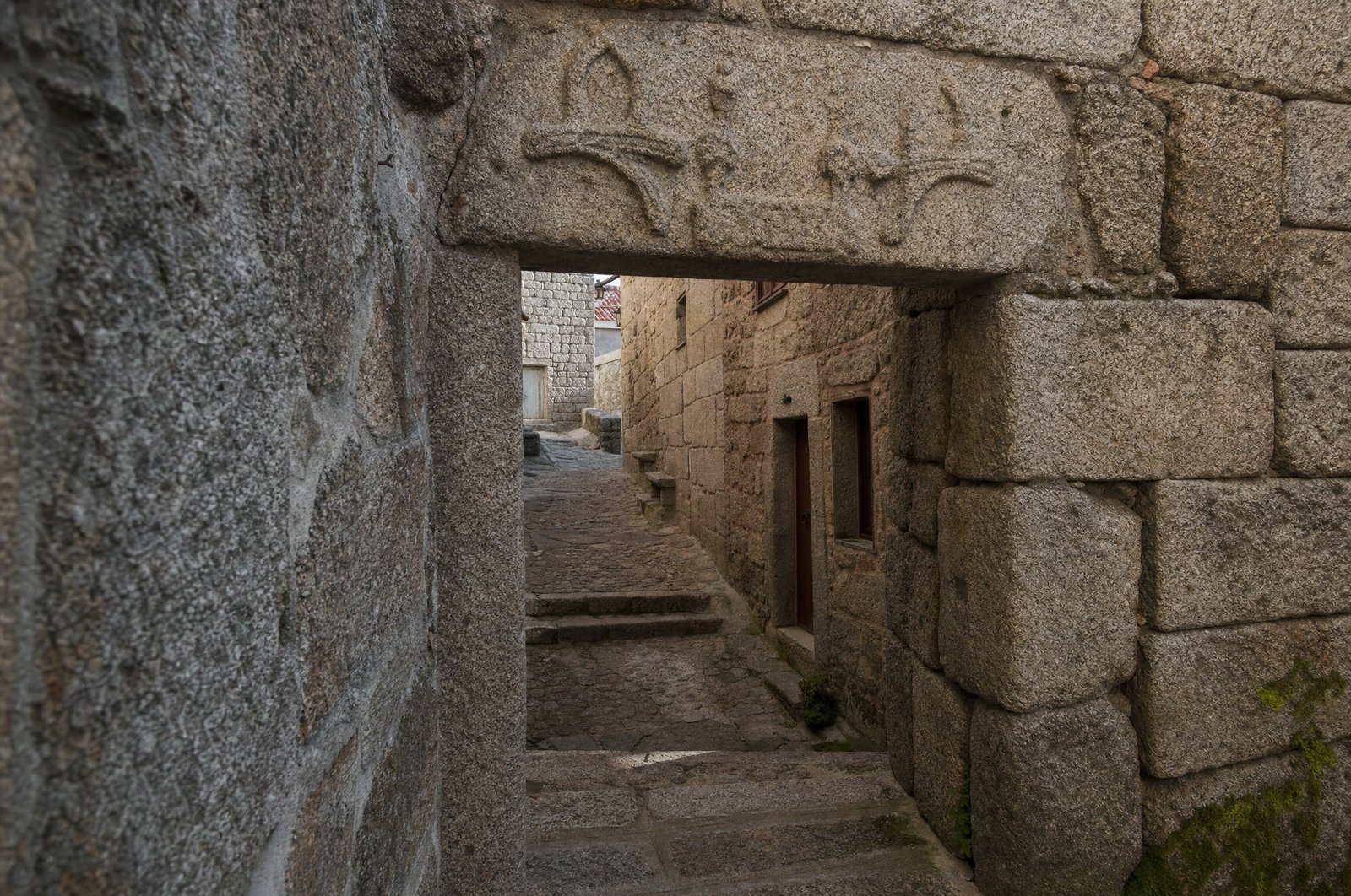 Ancienne porte de granit dans la Judiaria de Covilhã avec un linteau gravé à demi effacé, ruelle médiévale étroite, matière brute de la pierre, ambiance de fin d'automne, sans personnage