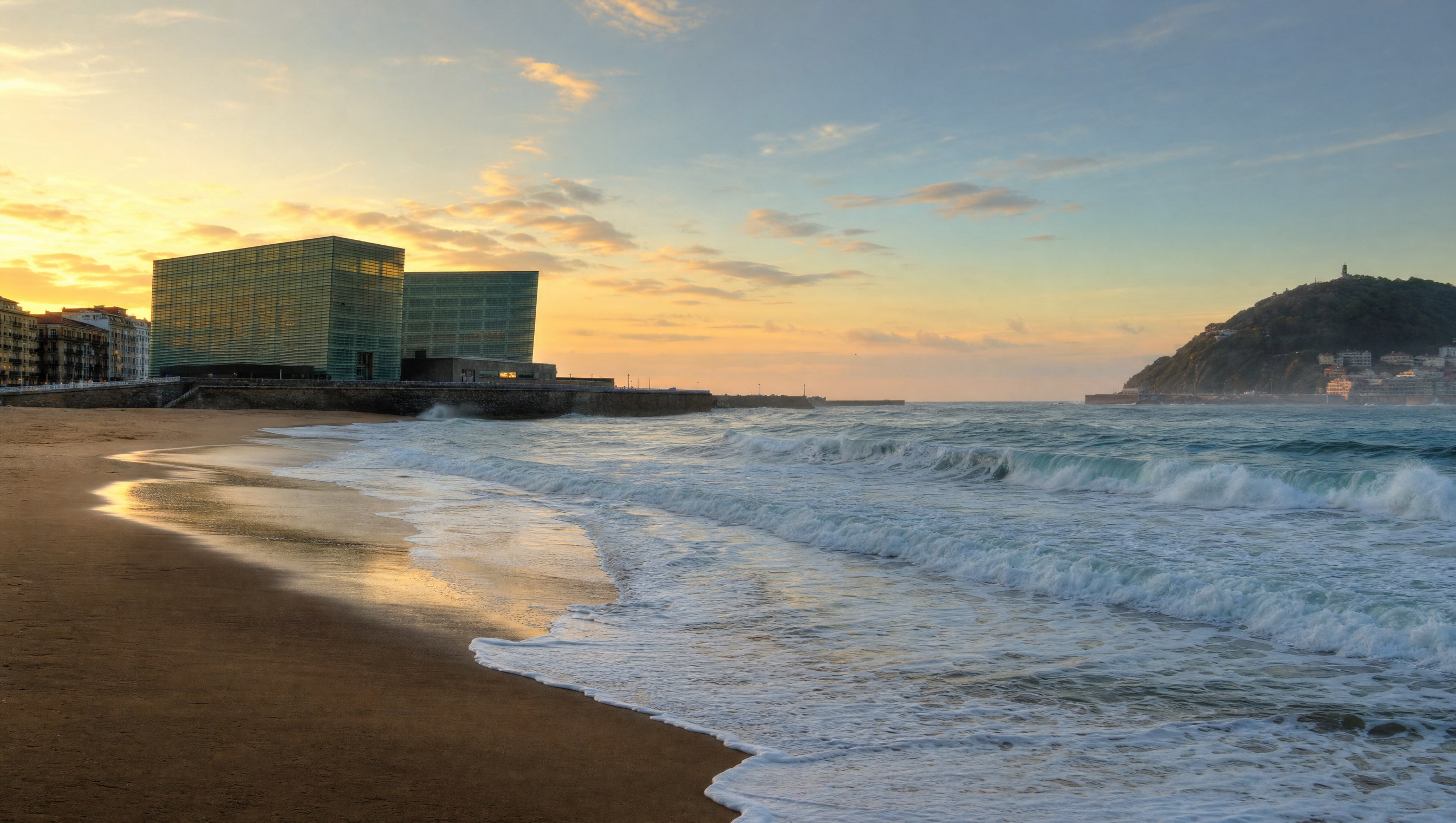 La plage de la Zurriola à Saint-Sébastien au lever du jour, vagues ourlées d’écume et les deux cubes de verre du Kursaal au bord de l’eau, aucune personne au premier plan, Pays basque, Espagne