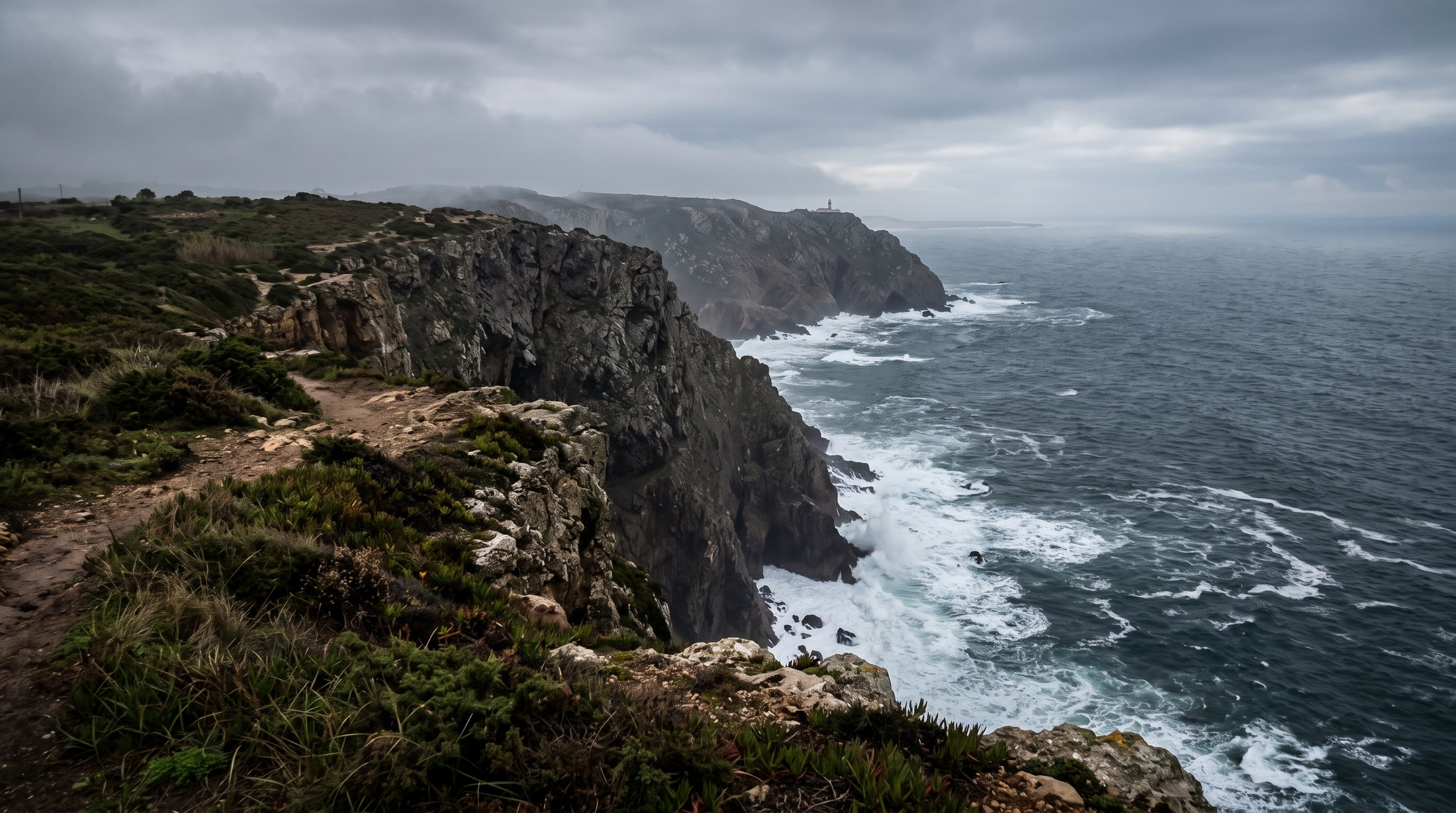 Falaise du Cabo da Roca plongeant de cent quarante mètres dans l'Atlantique, lande rase battue par le vent au bord du promontoire, lumière grise et brumeuse de fin d'automne, aucune personne