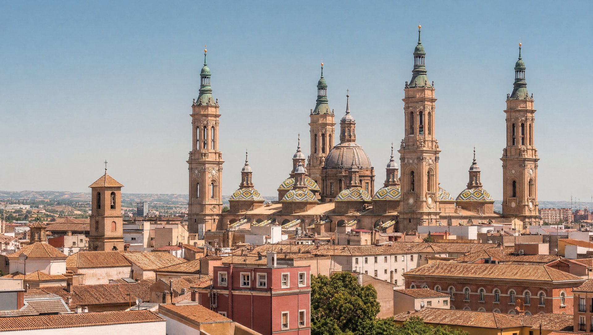 Les tours de brique rouge de la basilique du Pilar de Saragosse dominant les toits de la vieille ville sous un ciel d'été clair, ambiance de chaleur, aucun personnage