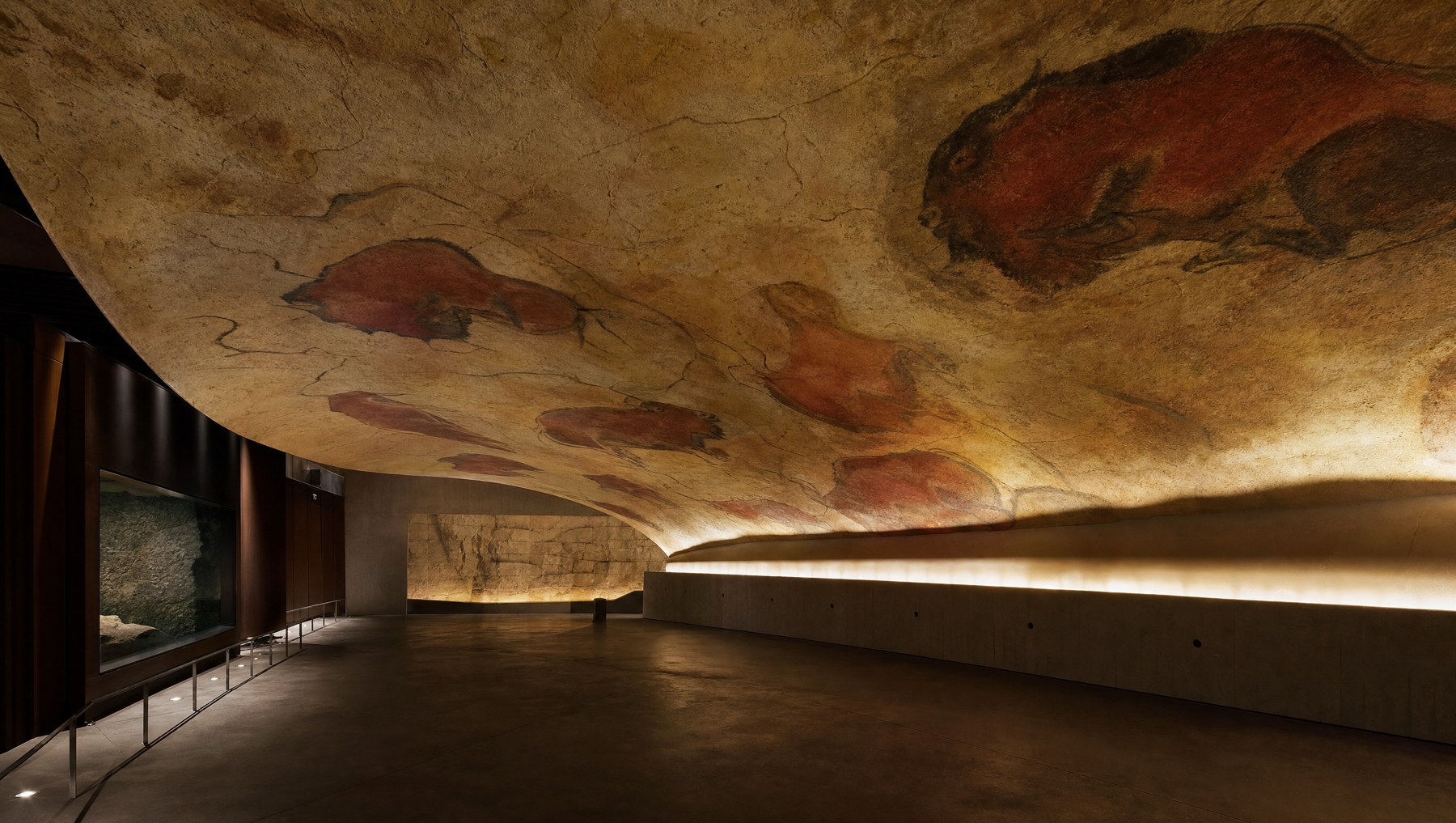 Salle d'exposition contemporaine en pénombre présentant la réplique moderne du plafond peint d'Altamira, grands bisons polychromes reproduits sur une voûte artificielle, éclairage muséal doux et rasant, aucune personne