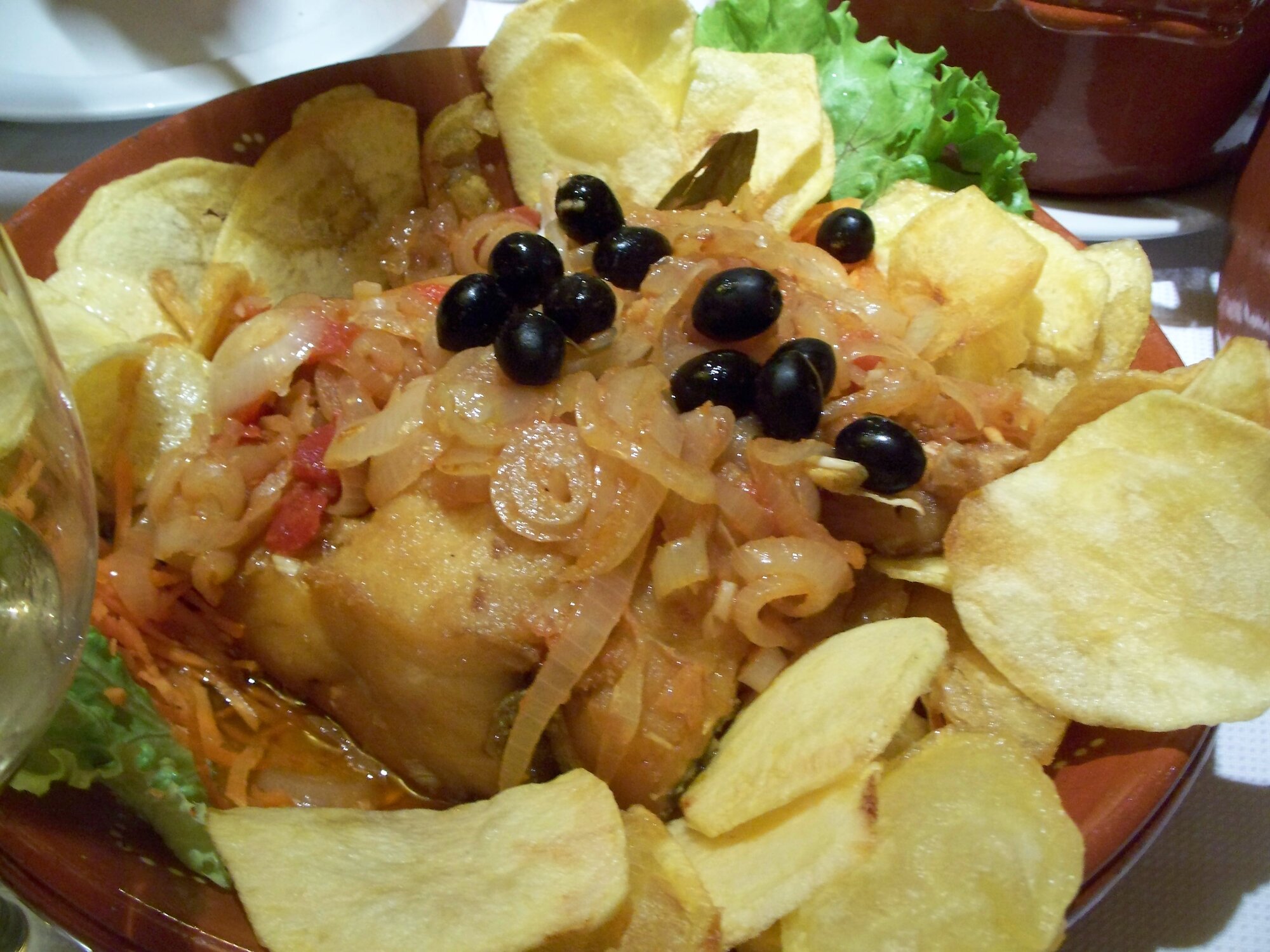 Bacalhau à Braga : morue frite dorée sur un lit d'oignons fondus et de fines pommes de terre frites, olives noires, servie dans un plat en terre cuite, Braga, Portugal