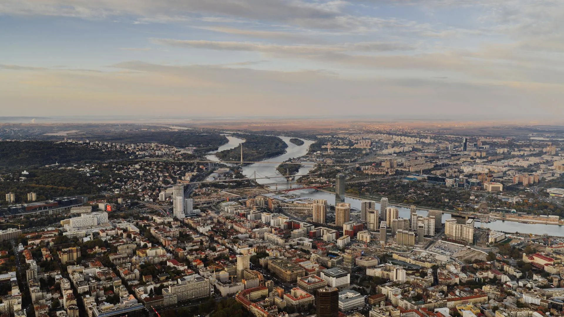 Aerial view of a city with multiple bridges crossing a winding river under a partly cloudy sky.