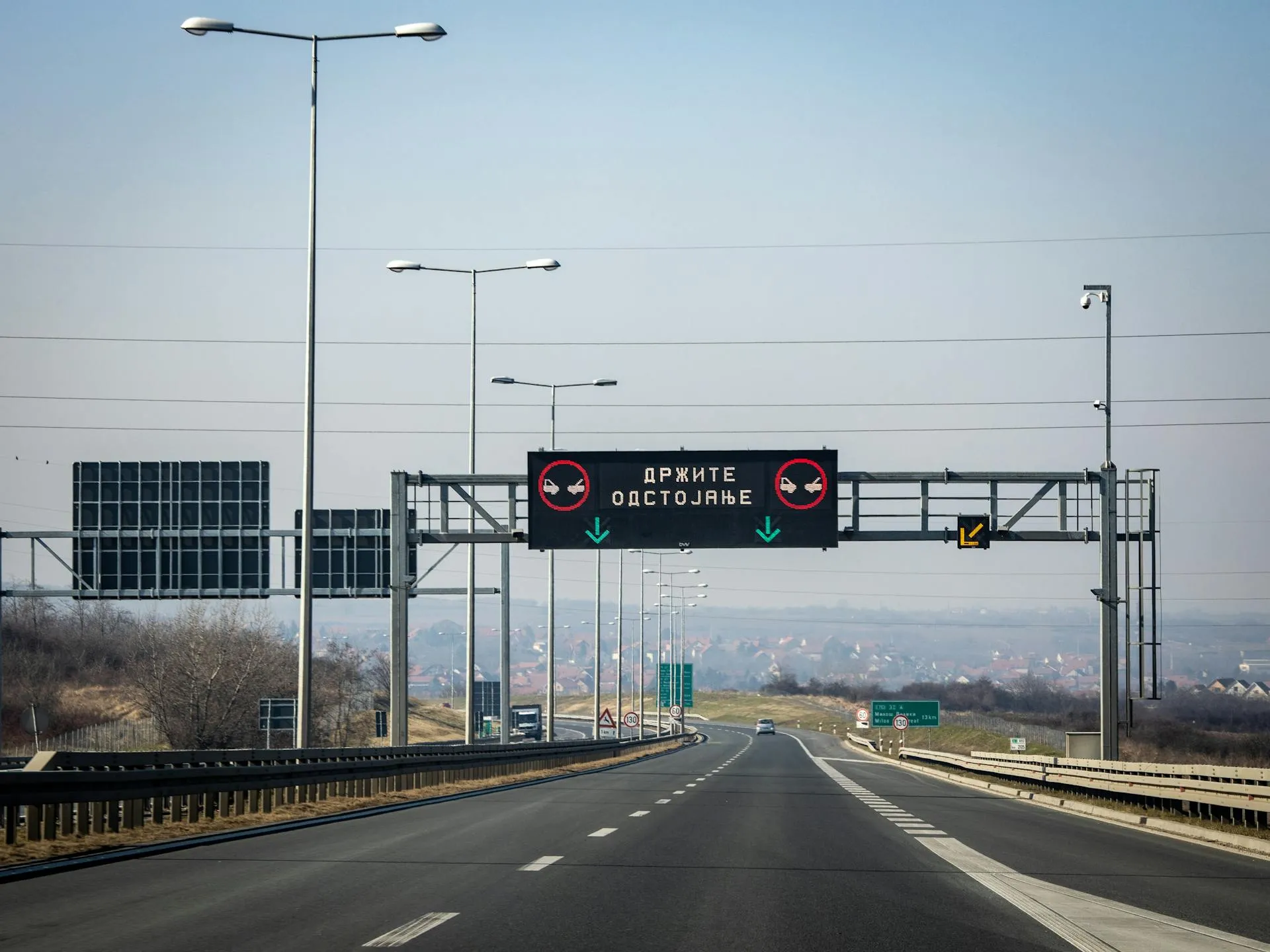 Empty highway with overhead electronic sign displaying a message in Serbian and green arrows pointing down.