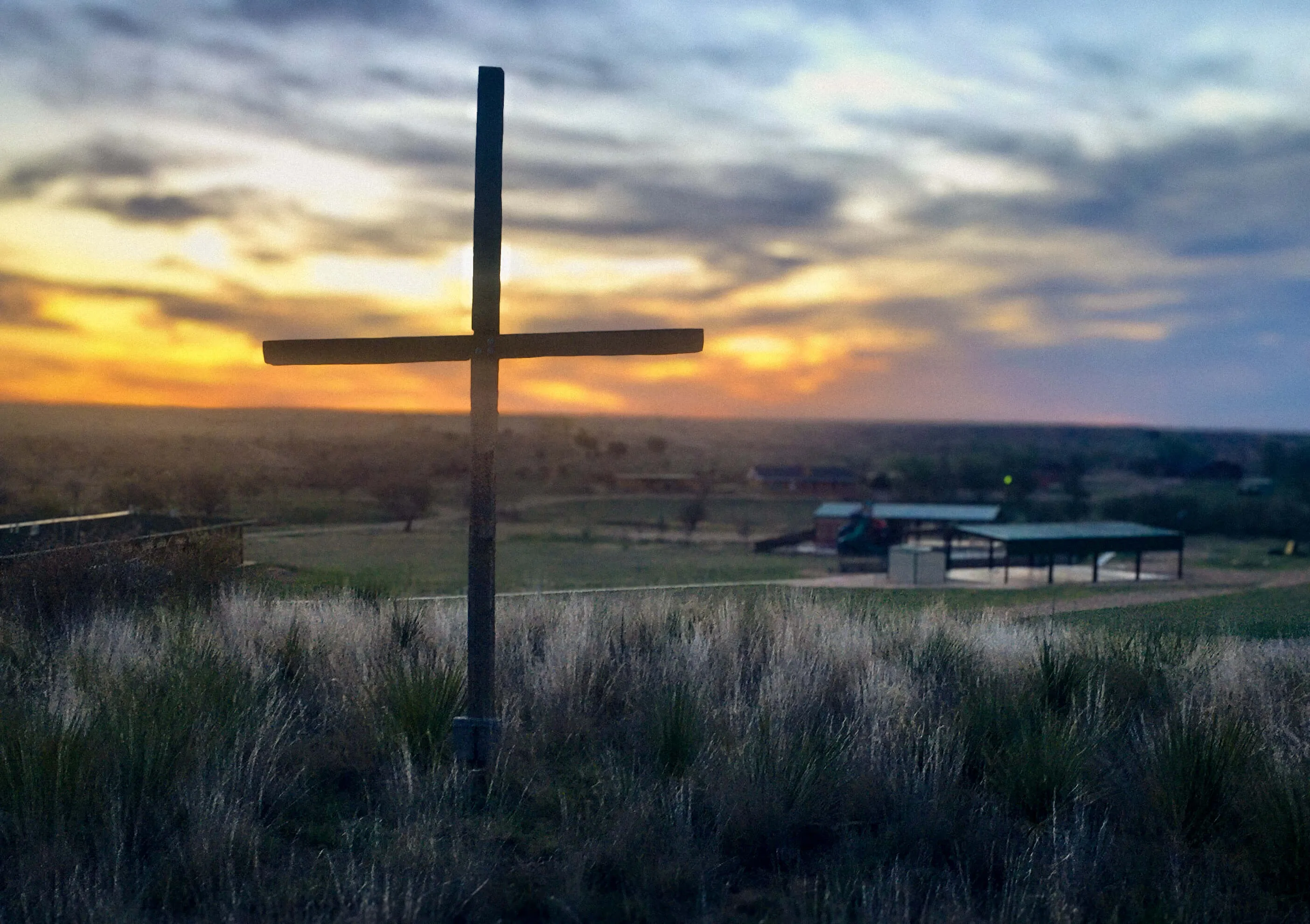 A cross and sunset photo with the High Plains Retreat Center in the background.